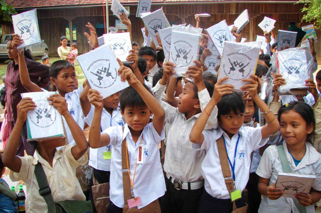 Enfants cambodgiens souriants en uniforme scolaire avec leurs cahiers neufs distribués par l'ONG AVEC, scolarisés grâce au parrainage